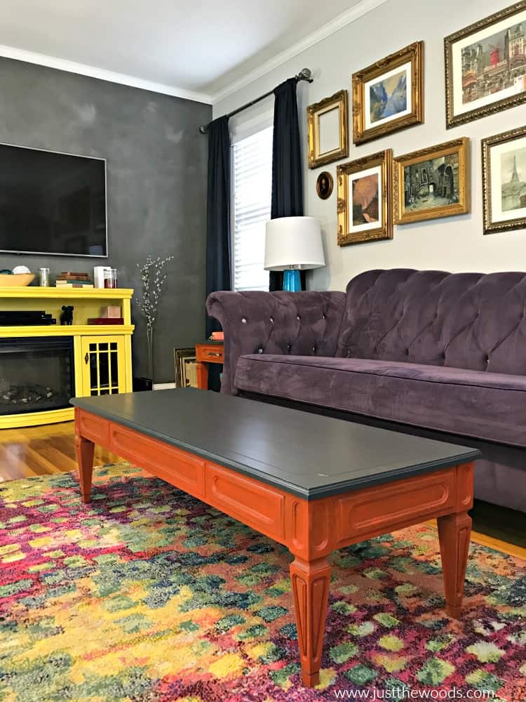 gray wall in living room, orange painted tables, yellow media console, purple sofa, repainted furniture