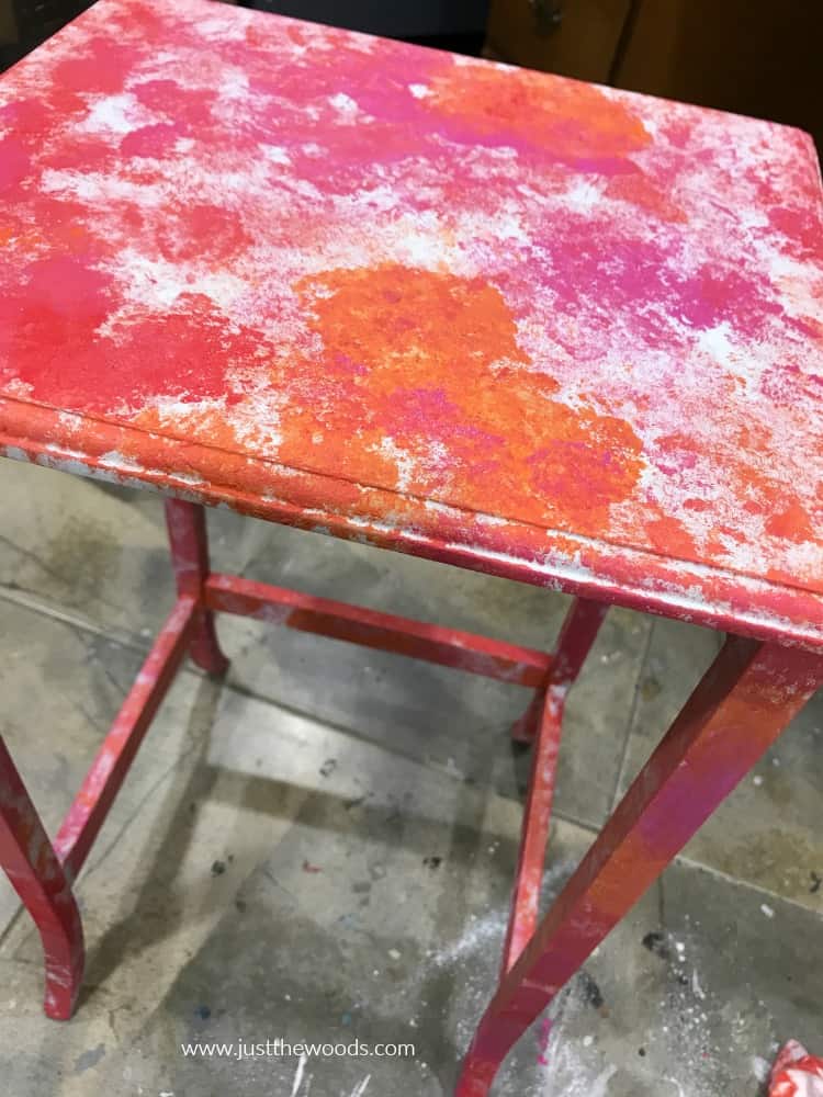 table painted with random splotches of red pink and orange paint