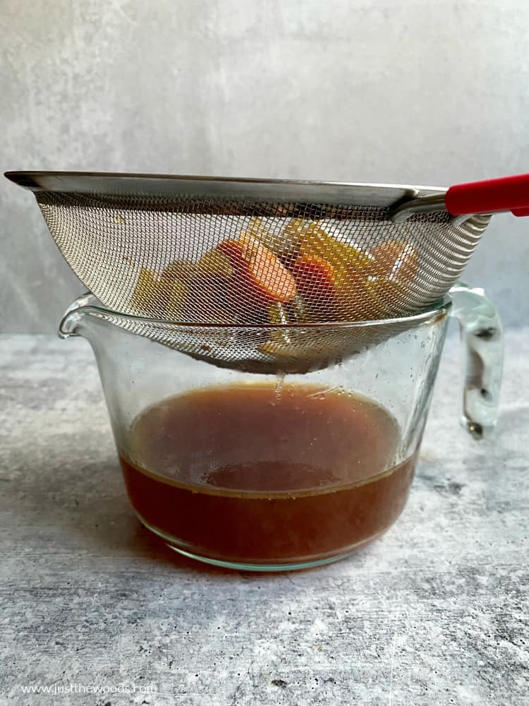 strain vegetables from bone broth over glass jar 