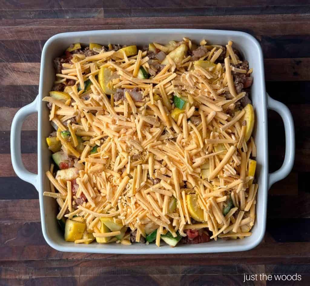 prepared gluten free squash casserole in dish with shredded cheese 