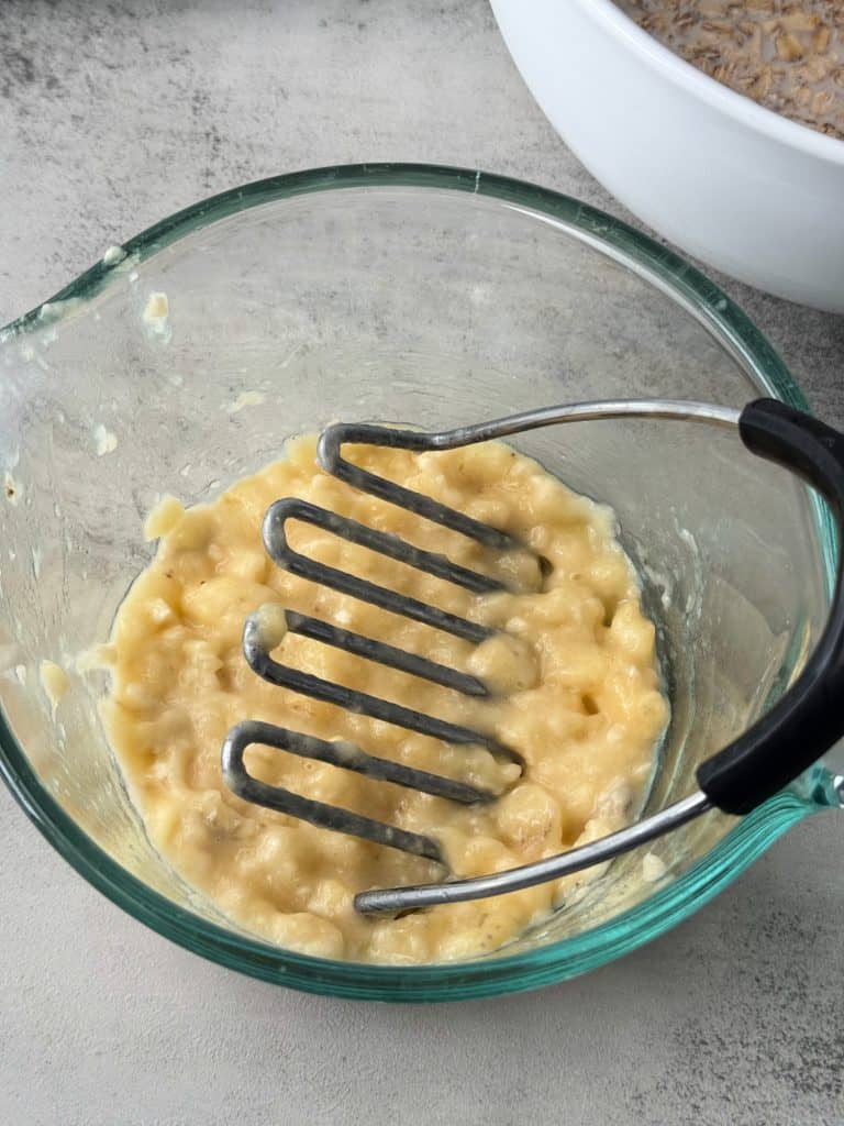 mashed bananas in bowl with potato masher 