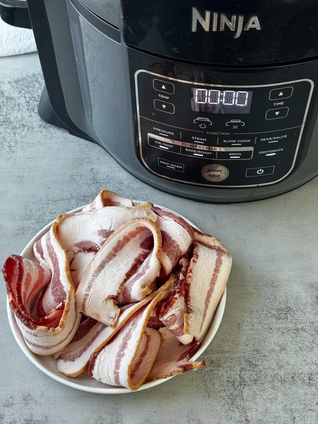 raw bacon on plate in front of ninja foodi air fryer