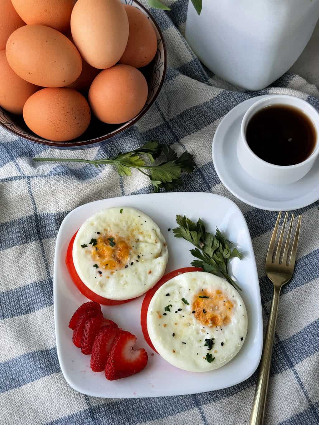 round cooked eggs on a plate with tomato and a sliced starwberry