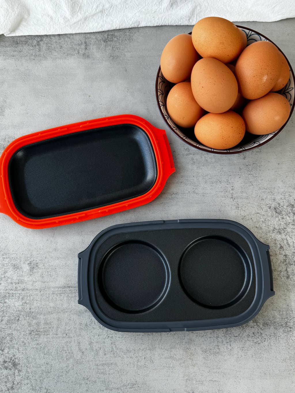 microwave egg cooker with red orange lid and black base, with a bowl of eggs