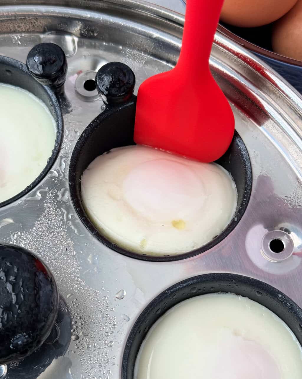 red spatula removing cooked poached egg from poaching cup