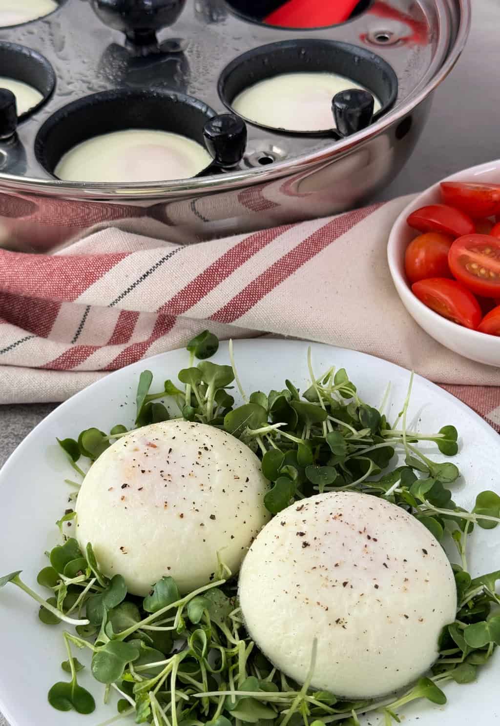 cooked poached eggs on plate with egg poacher pan behind it