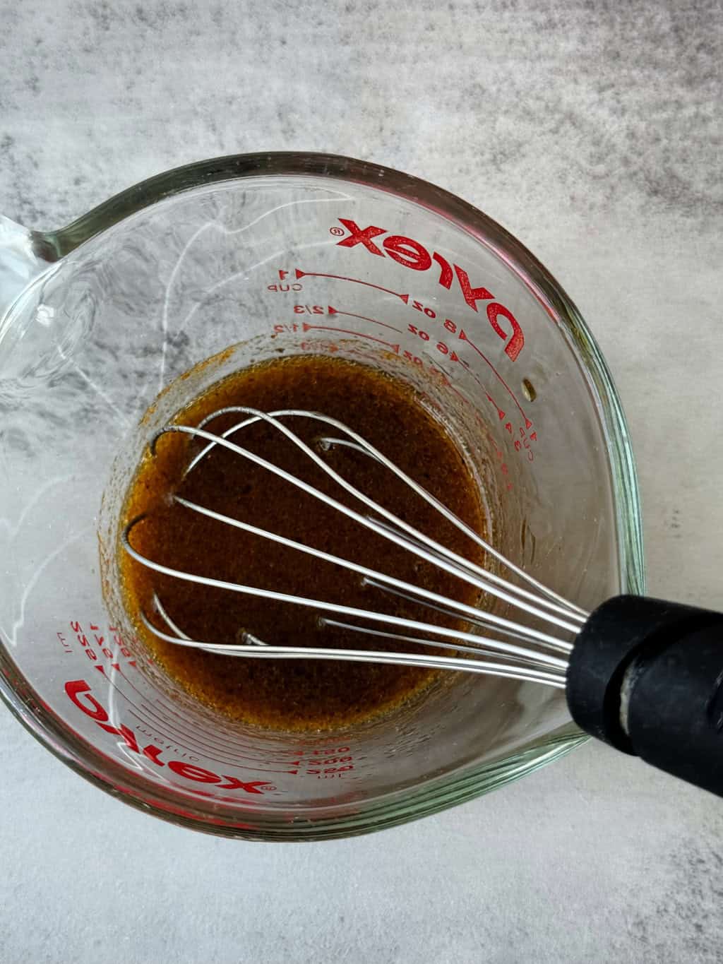 brown dressing liquid in glass bowl with wire whisk