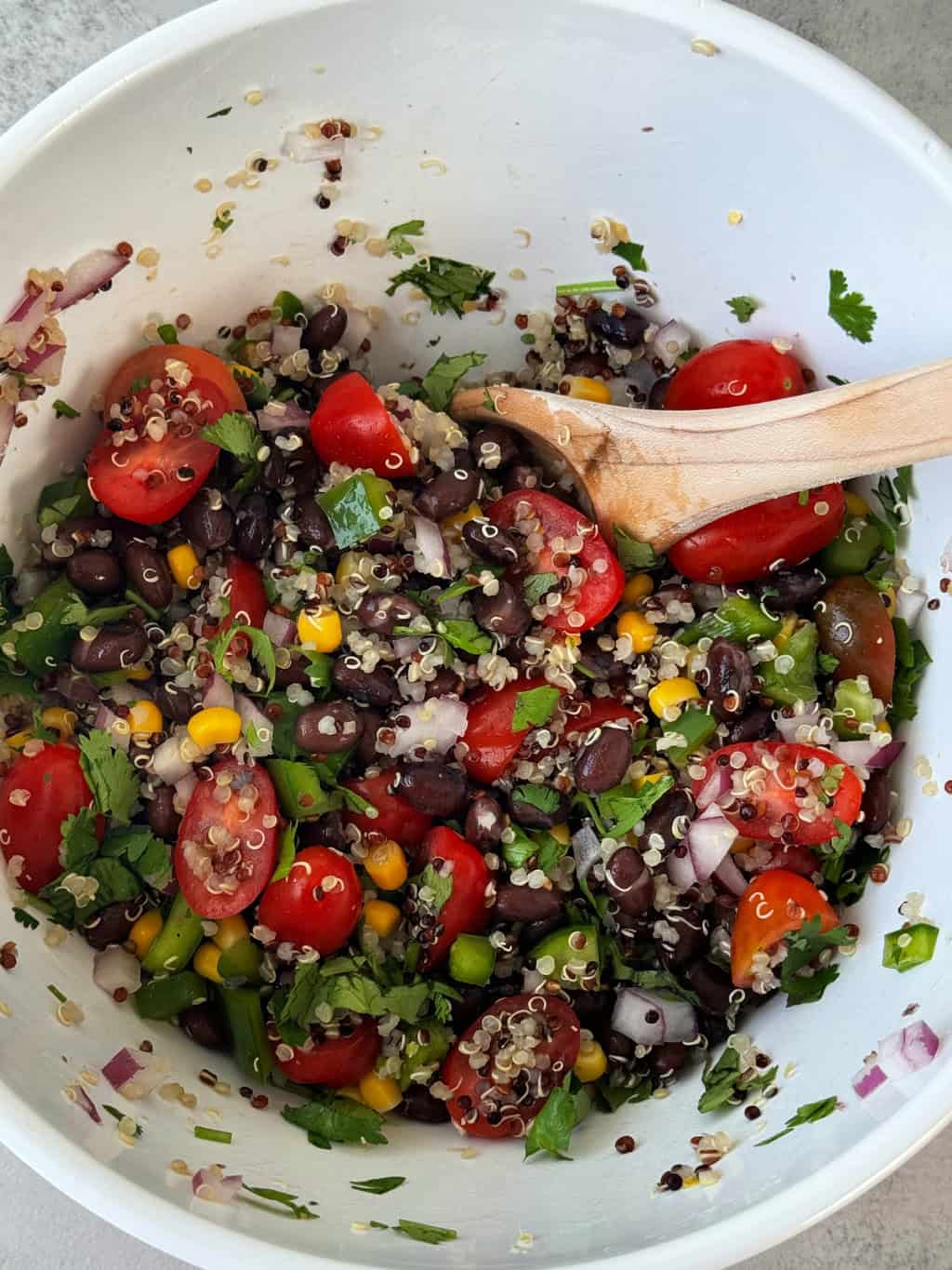 stir black bean quinoa salad ingredients with wooden spoon
