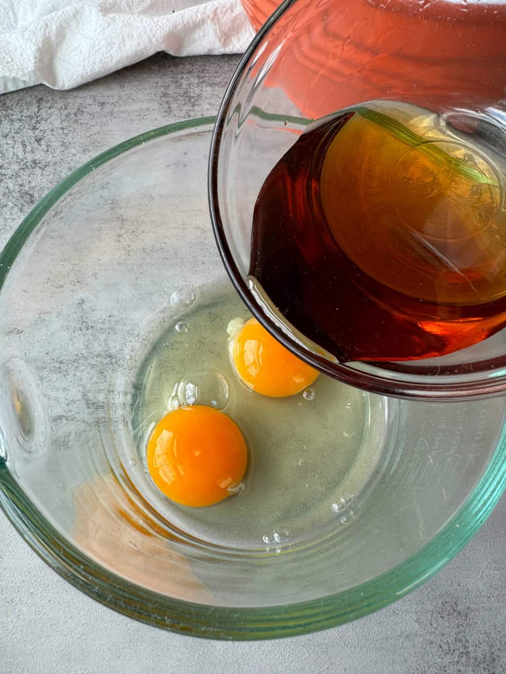 raw eggs in glass bowl and maple syrup being added