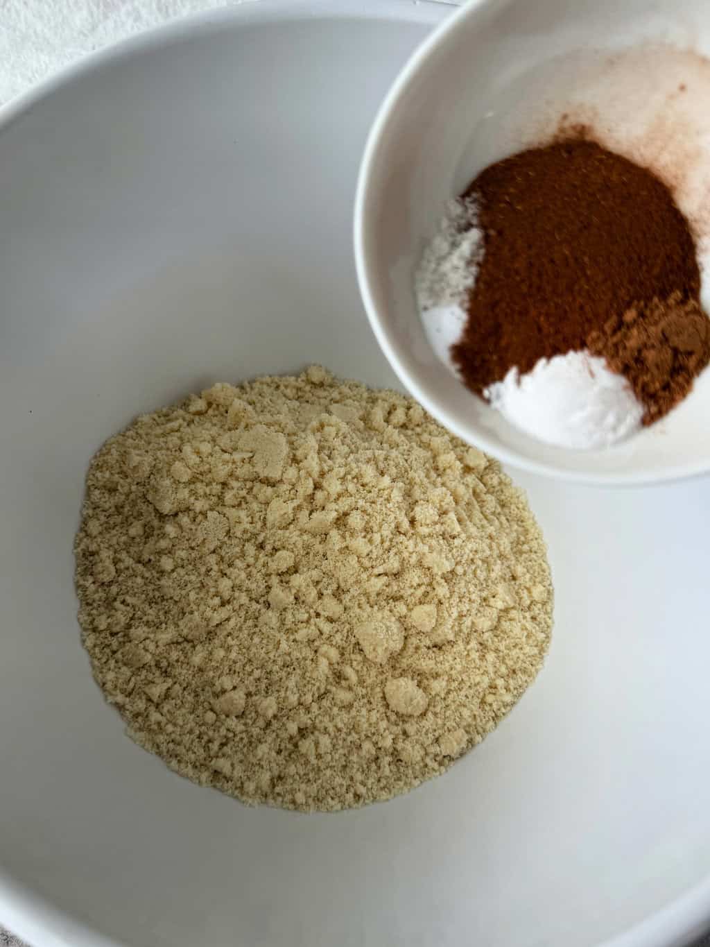 almond flour in large bowl with spices in small bowl being added