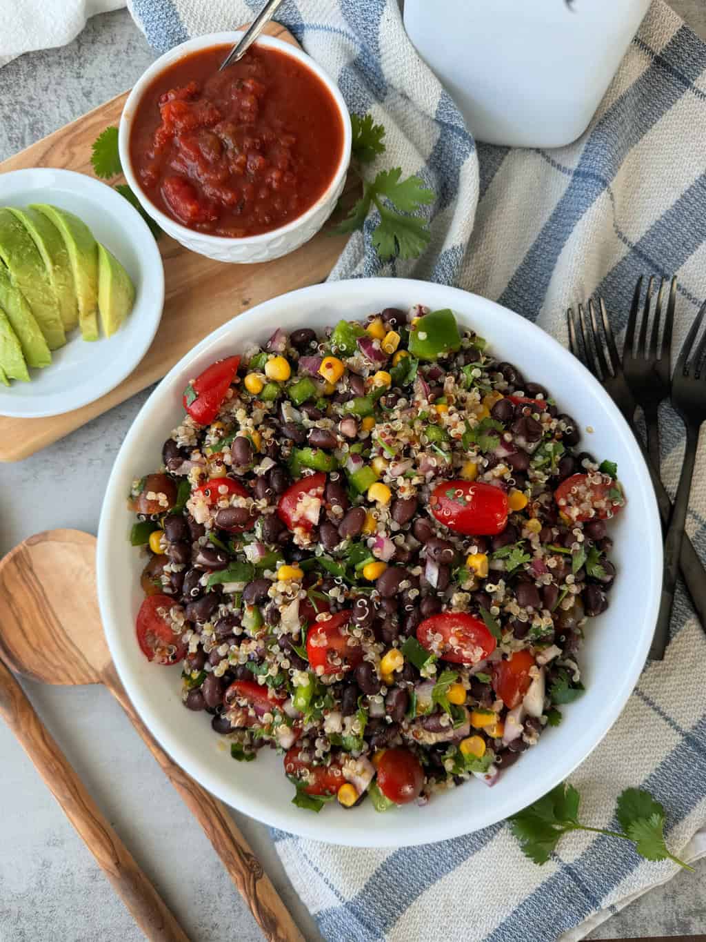 Black Bean and Quinoa Recipe with corn, bell peppers, tomatoes, cilantro and red onion in a white dish with a side of avocado and salsa