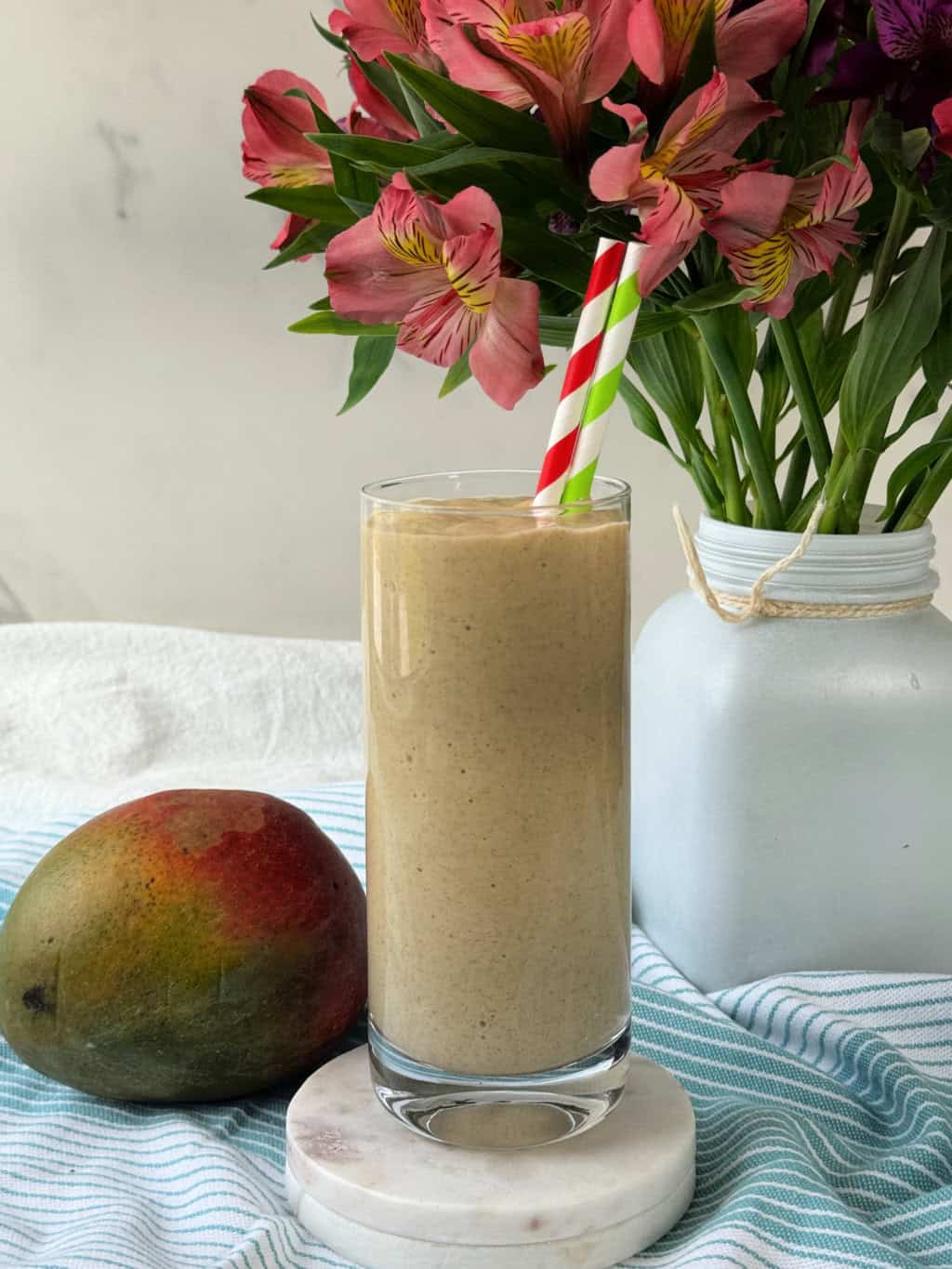 glass of creamy mango smoothie with protein on white stone coasters and two straws