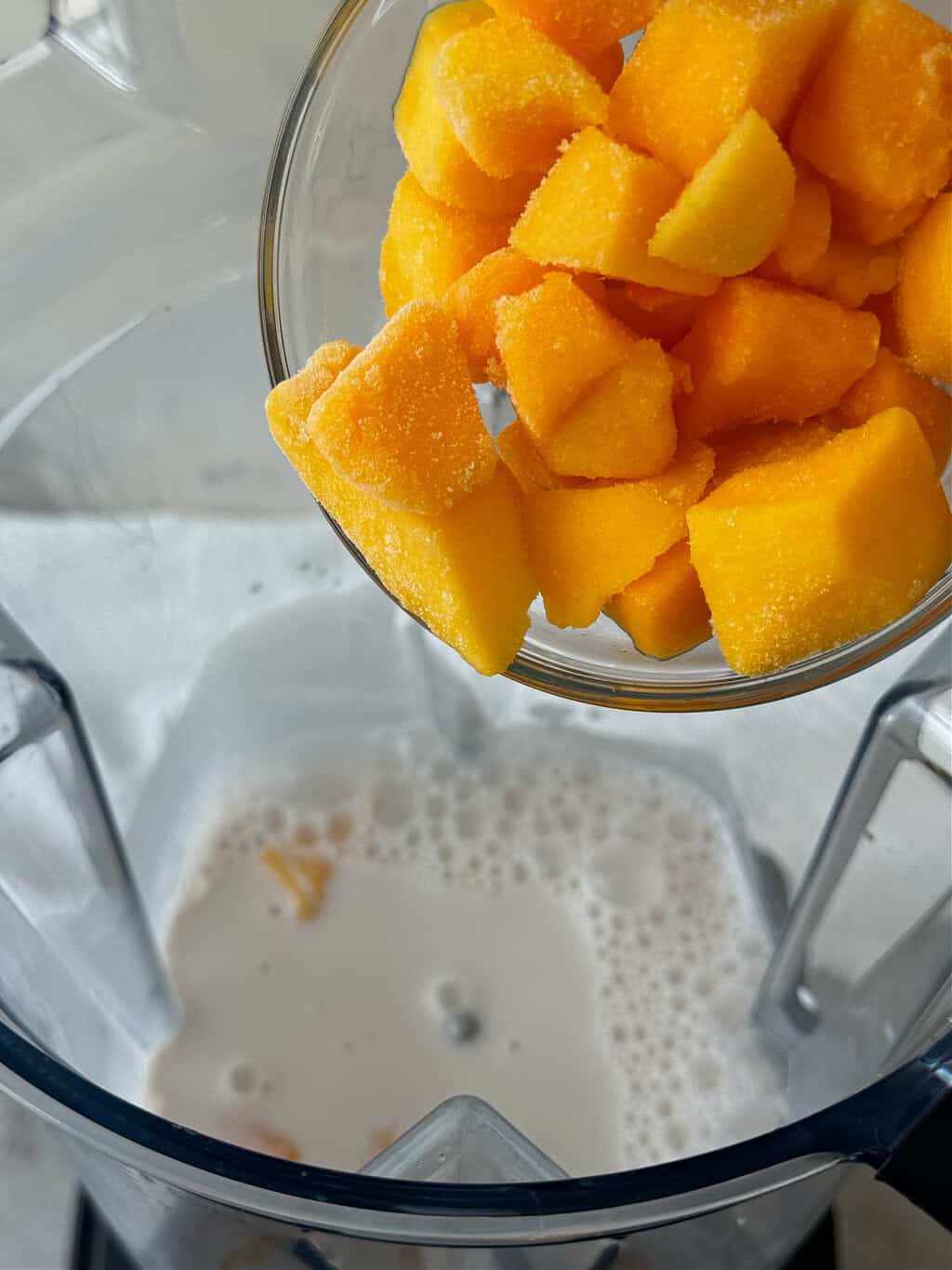 bright orange frozen mango into blender with dairy free milk