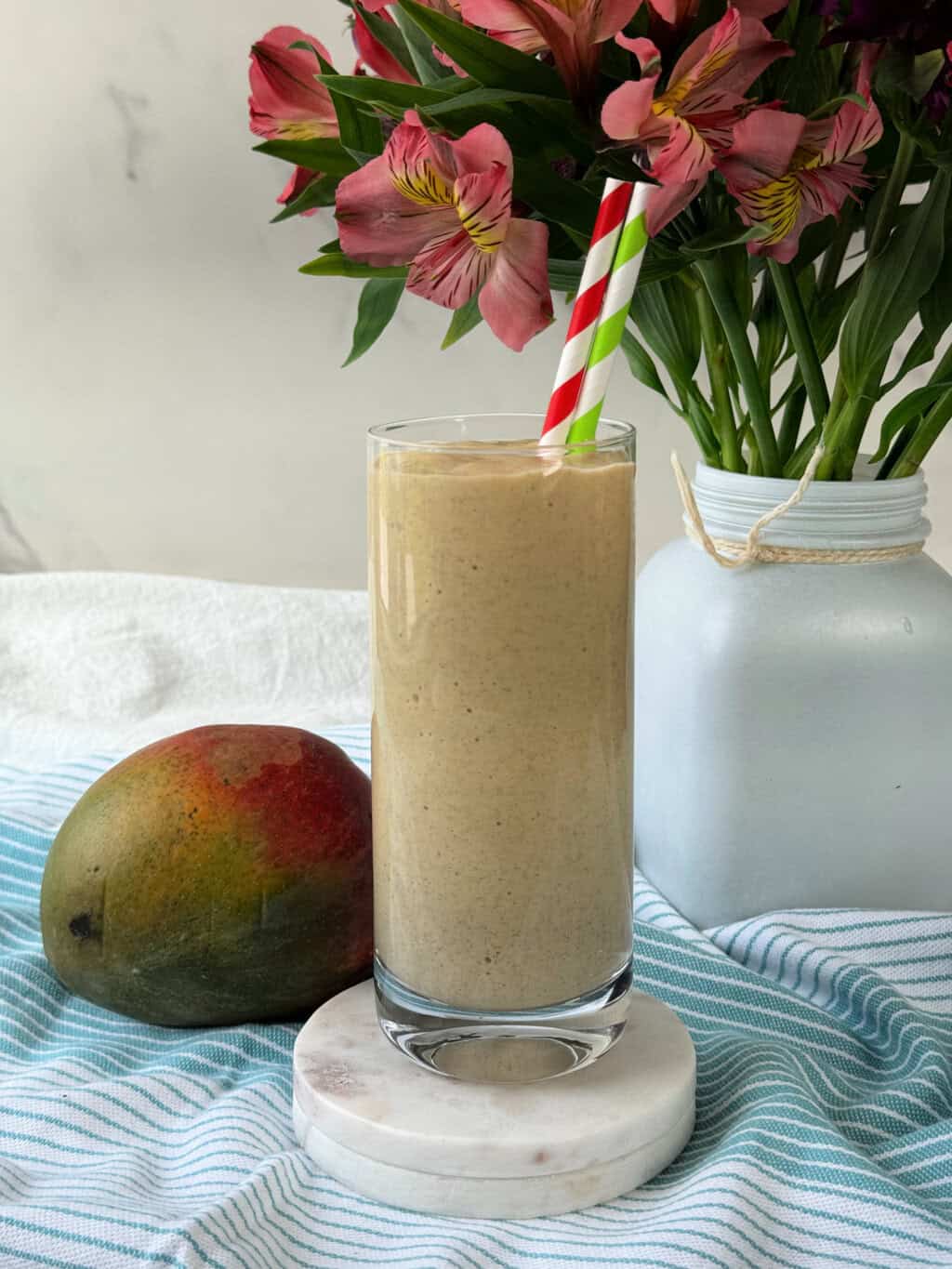 mango protein smoothie recipe in glass with fresh mango next to glass and flowers in background