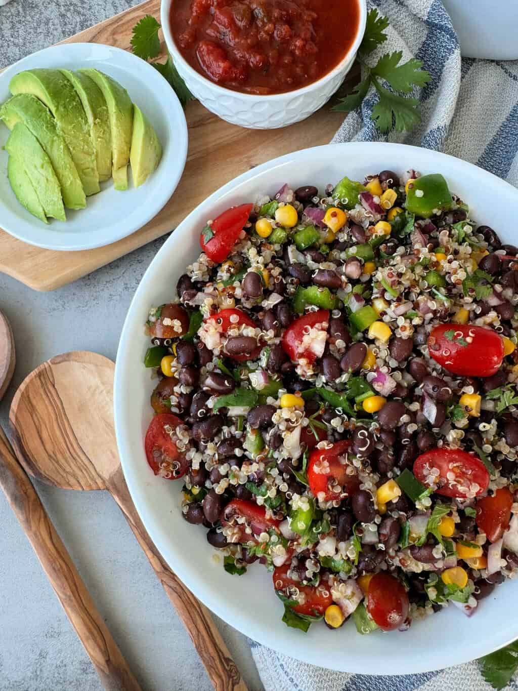 southwest quinoa salad in white bowl with tomatoes and a side of sliced avocado