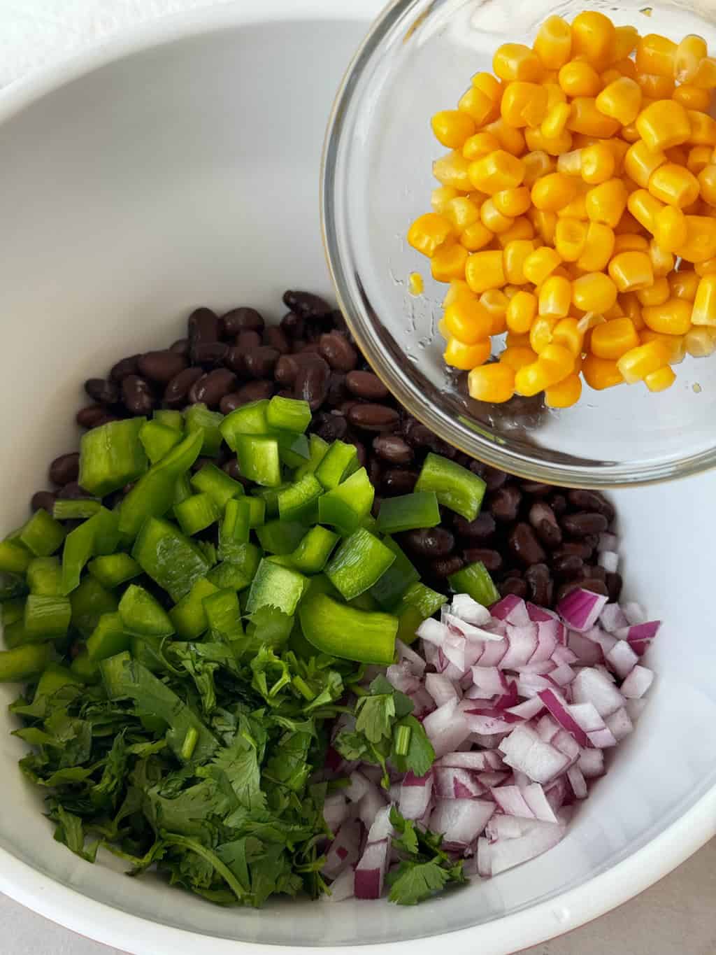 yellow corn going into bowl with peppers beans and onions